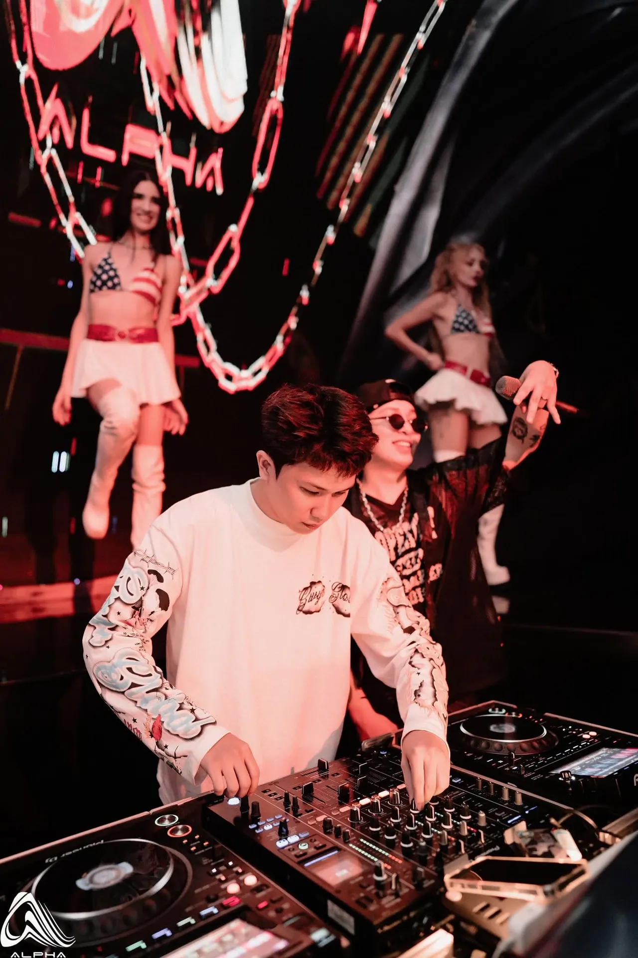 DJ chơi nhạc tại bốt DJ của ALPHA, vũ công biểu diễn trên bục phía sau dưới dây xích treo
