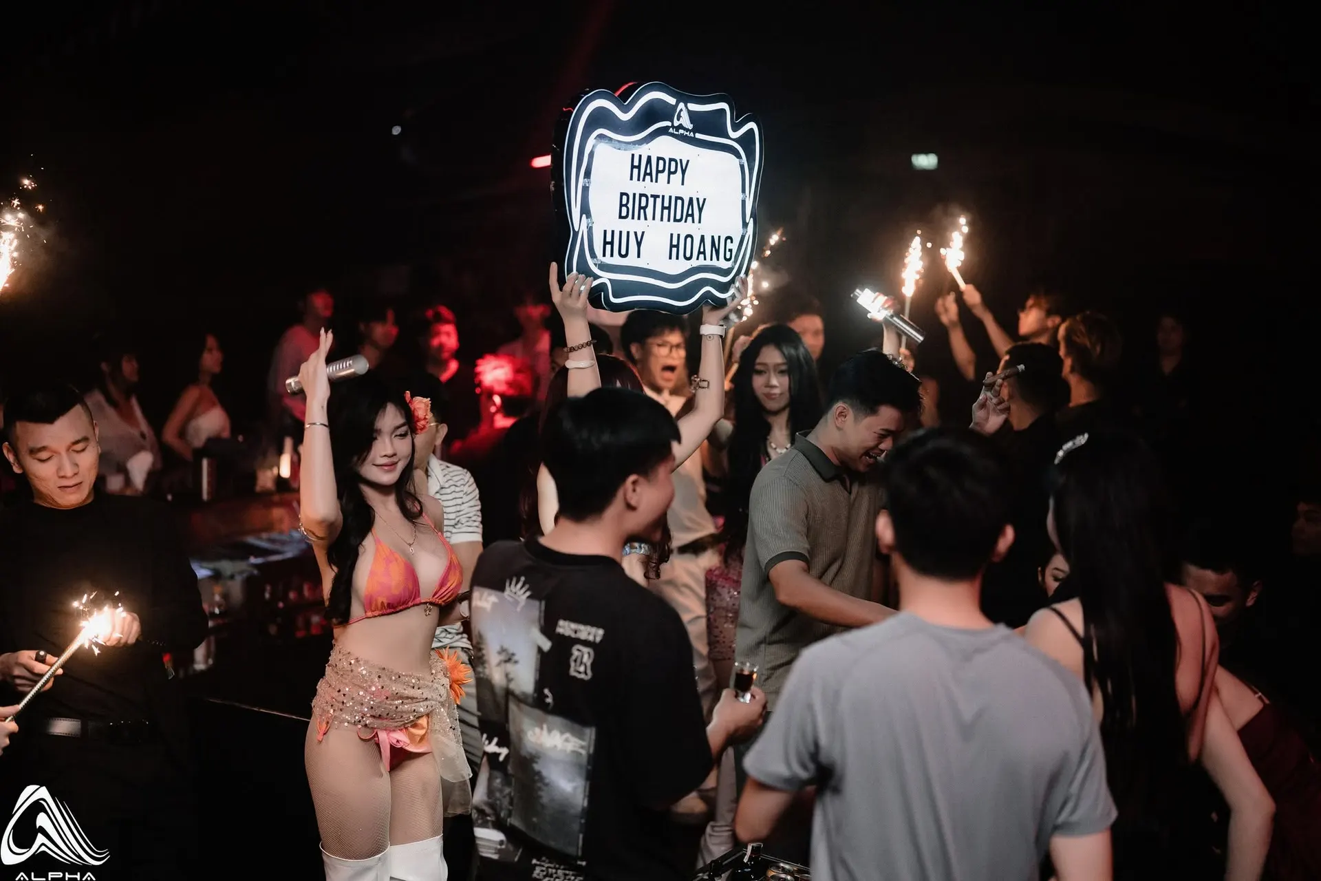 Bảng chúc mừng sinh nhật giơ cao giữa sàn ALPHA, pháo sáng và khách vây quanh
